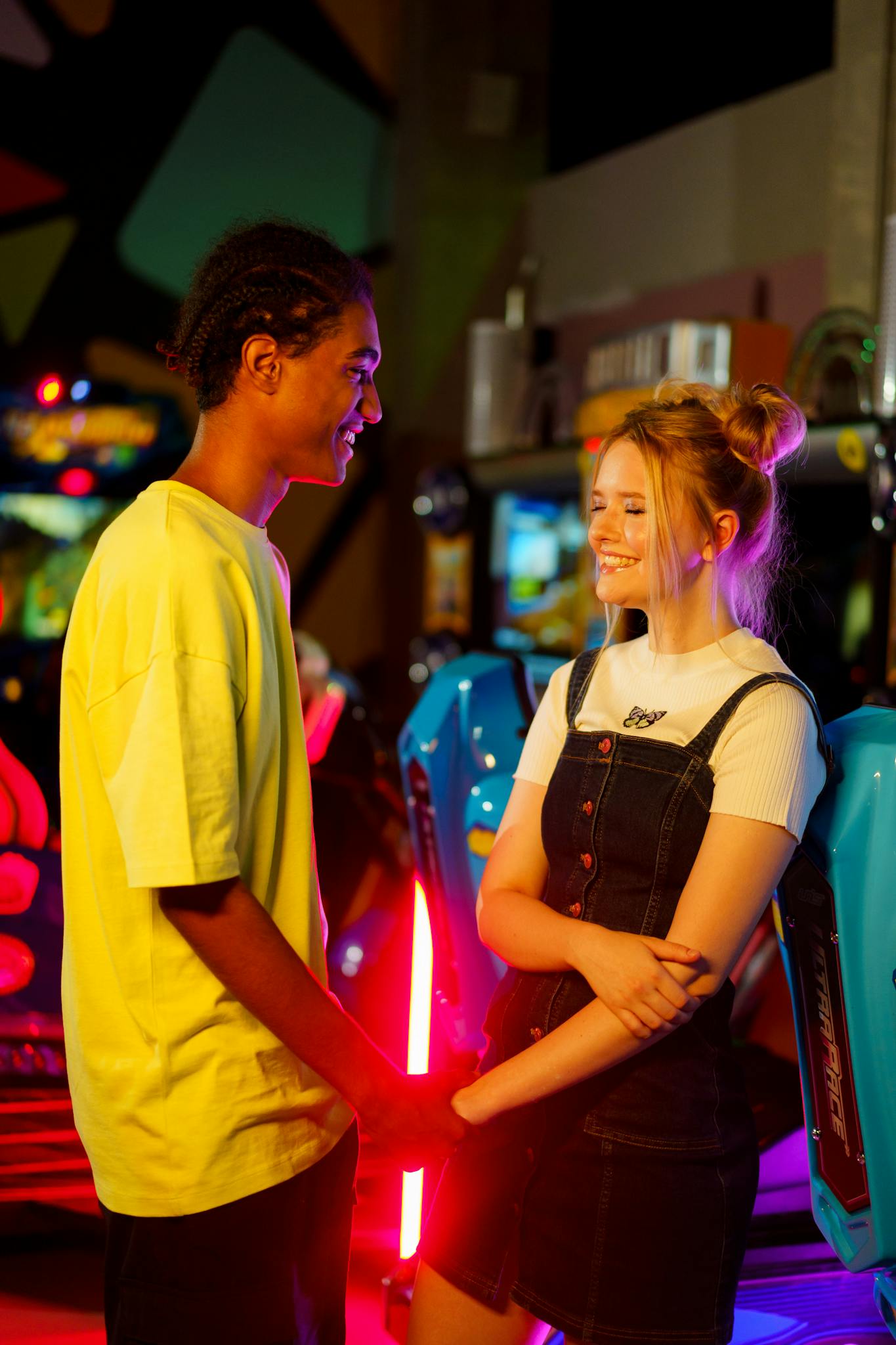 A joyful couple holds hands and smiles warmly in a colorful arcade setting.