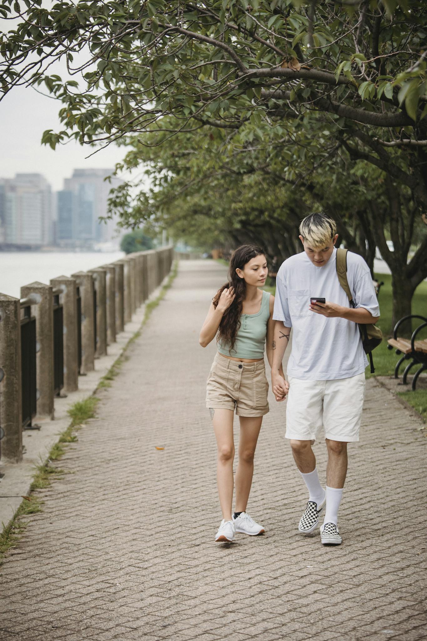 A young couple holding hands and walking outdoors, enjoying leisure time by the riverside.